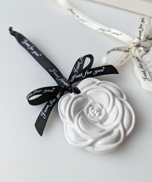 White ceramic rose-shaped object with a black ribbon on a white background